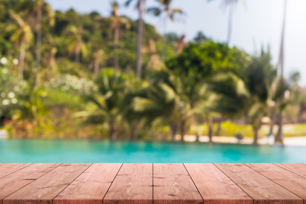 Piano d'appoggio di legno vuoto e piscina vaga nella località di soggiorno tropicale nel fondo dell'insegna di estate.