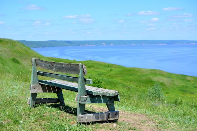 An empty wooden bench on top of hill with green grass and Volga river on background