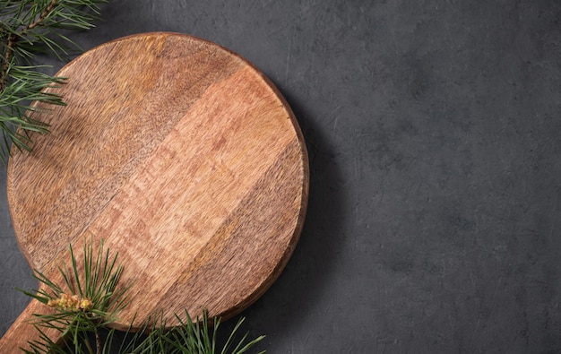 Empty wooden board on dark texture background with fir tree branch Cutting board for serving food or preparing homemade and healthy food Top view and copy space