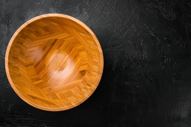Пустая деревянная чаша с копировальным пространством для текста или еды, вид сверху, плоская планировка, на фоне черного темного каменного стола
