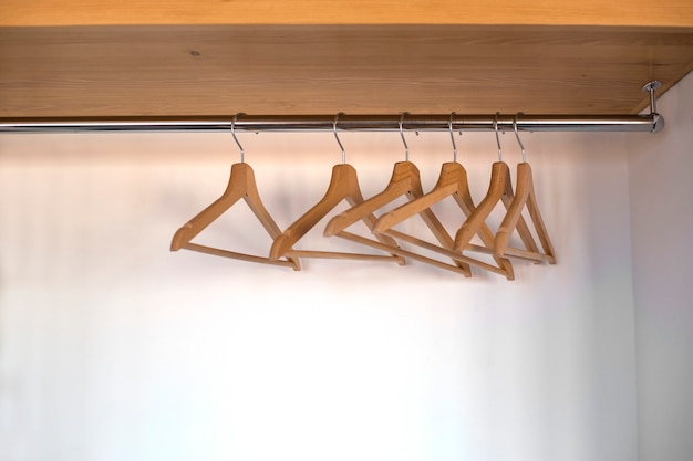 Empty wooden hangers hang in a closet on a metal rail