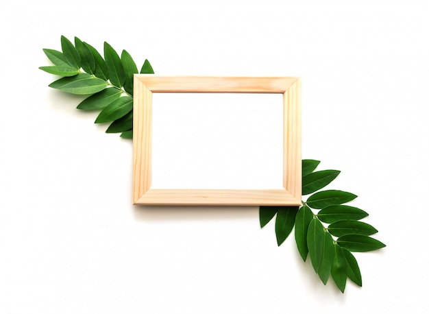 Empty wooden photo frame with green leaves around on white background