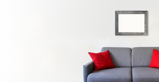 Empty wooden picture frame on a white wall above a sofa. Minimalist interior background. Horizontal banner