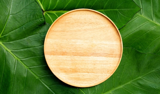 Empty wooden plate on taro leaves. Top view