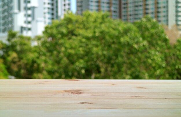 Empty wooden table at the balcony with blurry green foliage and modern building in background