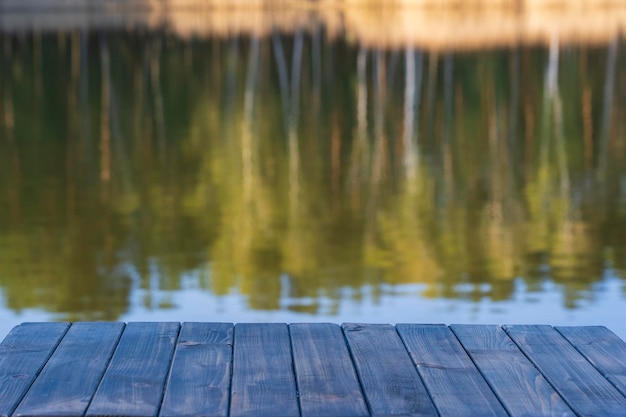 Tavolo in legno vuoto e vista sullo sfondo sfocato del lago calmo vicino alla foresta primaverile per l'esposizione del prodotto