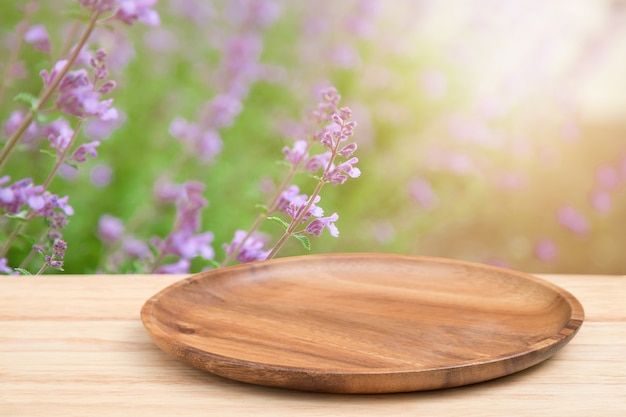 Empty wooden tray on perspective wooden table on top over blur flower background.