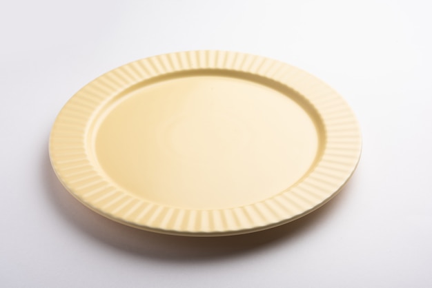 Пустая желтая керамическая круглая тарелка с декоративной каймой на белой поверхности