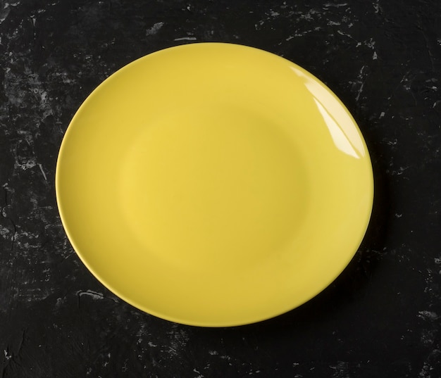 An empty yellow plate on a black textured background.