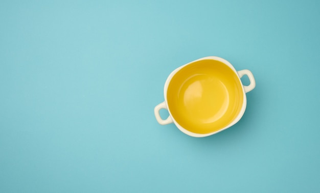 Empty yellow soup plate on a blue background, top view, copy space