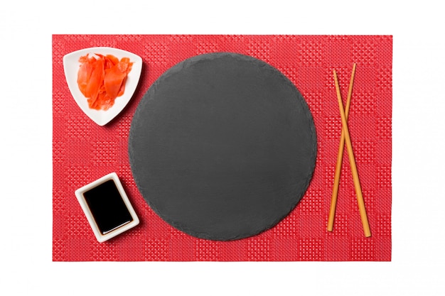 Emptyround zwarte leisteen plaat met stokjes voor sushi en sojasaus, gember op rode mat sushi. Bovenaanzicht met kopie ruimte voor u ontwerpen