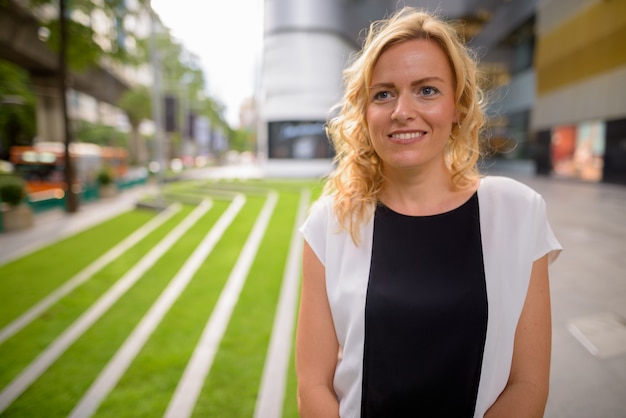 Foto en portret van mooie blondeonderneemster die in openlucht glimlachen denken