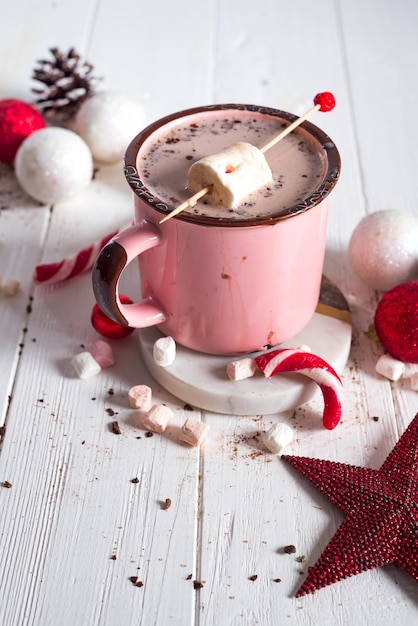 Enamel cup of hot cocoa with mini marshmallows and candy canes with pine 