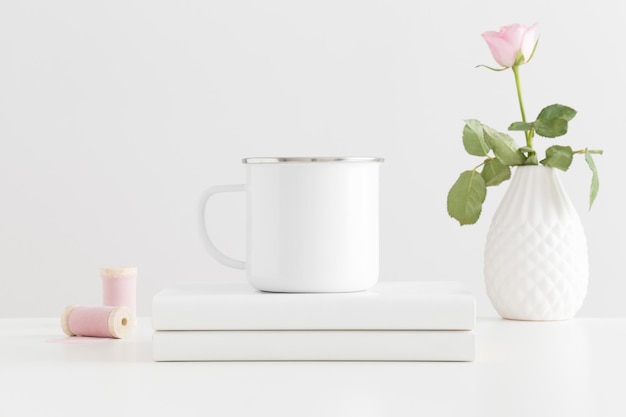 Enamel mug mockup with a pink rose and books on a white table