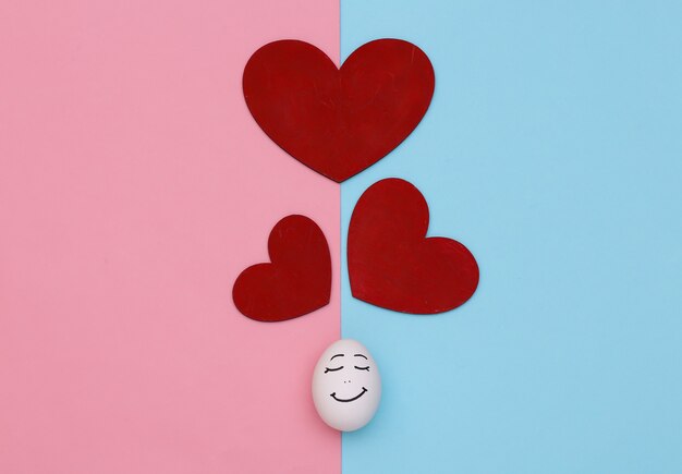 Влюбленное лицо яйца и сердце на сине-розовом пастельном фоне. День святого Валентина. Вид сверху