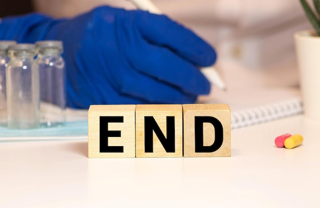 Photo the end word sign with wooden blocks on a table with hands in medical gloves