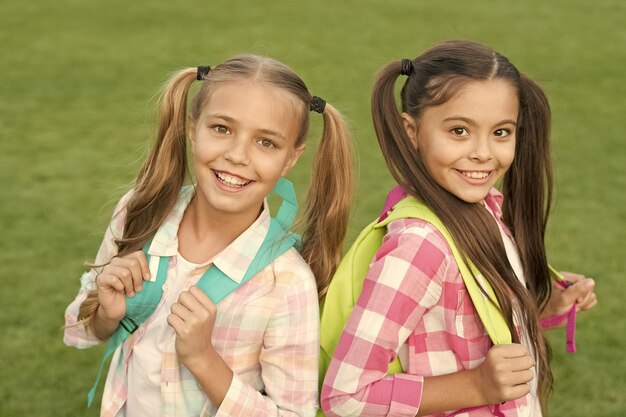 Photo ending of school year cheerful smart schoolgirls happy schoolgirls outdoors small schoolgirls with backpacks september vacation is over back to school cute schoolgirls with long ponytails