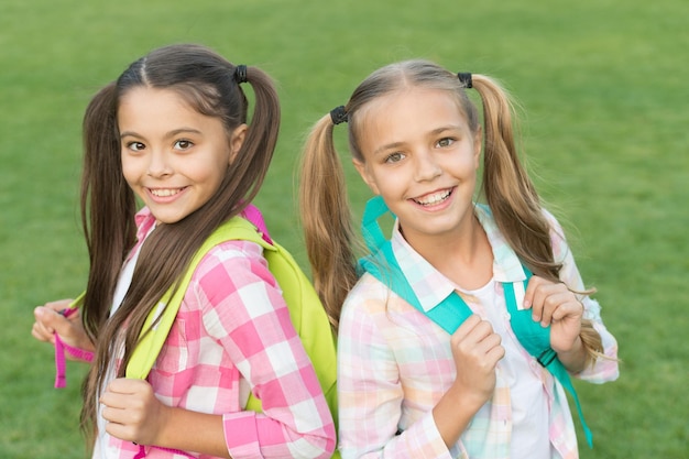 Photo ending of school year cheerful smart schoolgirls happy schoolgirls outdoors small schoolgirls with backpacks september vacation is over back to school cute schoolgirls with long ponytails