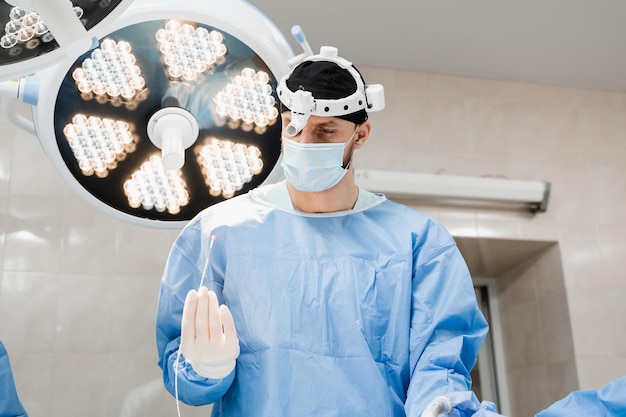 Эндовенозная лазерная коагуляция для лечения варикозного расширения вен Сосудистый хирург держит EVLT Красное лазерное оптическое волокно для лечения тромбофлебита тромбоза ног в операционной