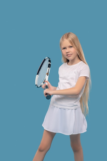 Endurance, training. girl with long blond hair in sportswear\
training with tennis racket in studio photo