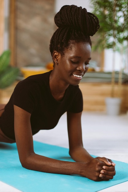 Enduring afro american woman with dreadlocks standing in elbow plank through pain closeup training on gymnastic mat in decorated studio Muscle strengthening pumping up fitness keeping body fit