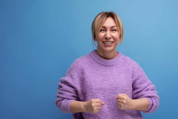 Energetic blond young woman in purple hoodie on blue background with copy space