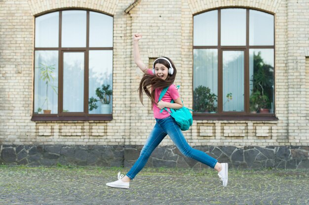 Energetic child girl jumping dancing listening music headphones, happy dance concept.