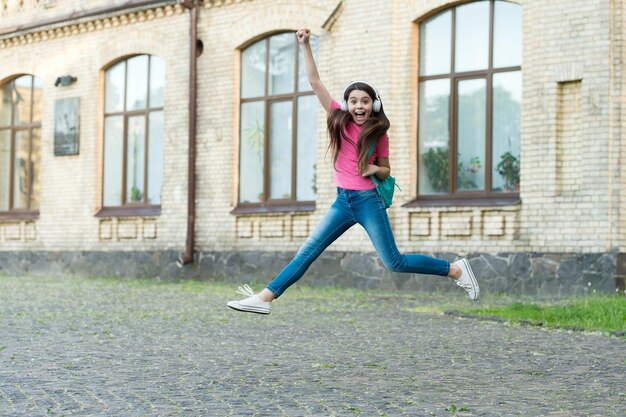 에너지 넘치는 어린 소녀가 춤추는 음악 헤드폰을 점프하며 결코 개념을 멈추지 않습니다.