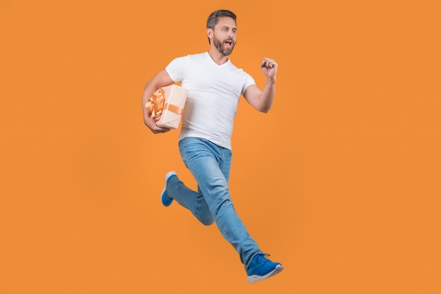 Energetic courier guy running with present box in midair yellow background Courier service
