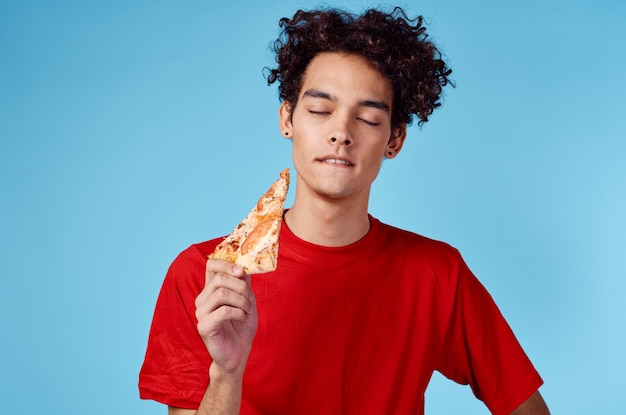 Photo energetic guy with a slice of pizza having fun on a blue background and a red tshirt high quality photo