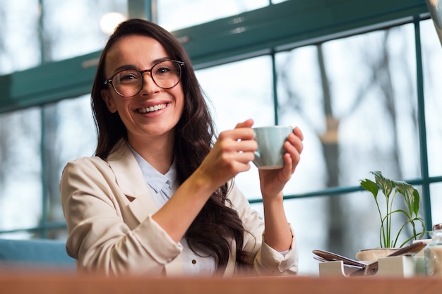 Energetic in hands. Enthusiastic pleasant joyful woman posing at the cafe while smiling and staring at camera