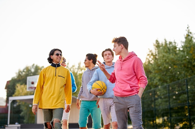 Энергичные, здоровые подростки веселятся, болтают перед игрой в баскетбол