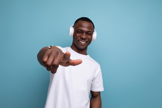 Energetic joyful darkskinned young american guy in a white tshirt listens to a podcast in headphones