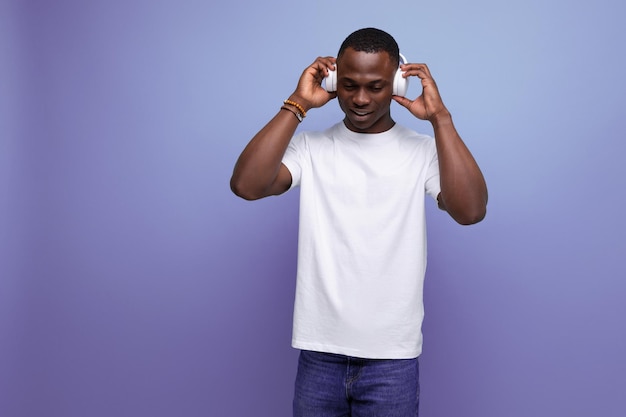 Energetic joyful darkskinned young american guy in a white tshirt listens to a podcast in headphones