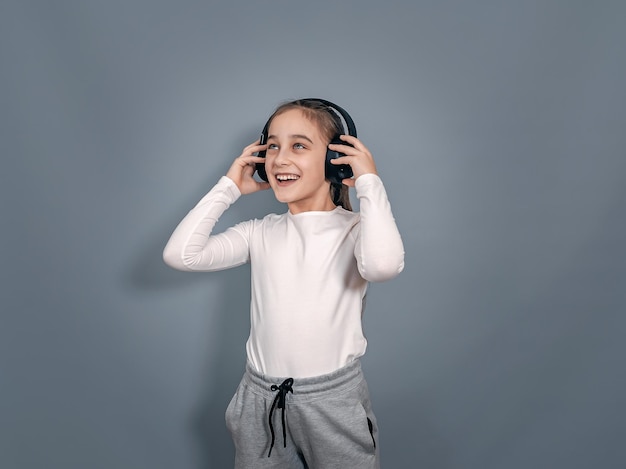 Energetic little girl in headphones holds headphones listens to music