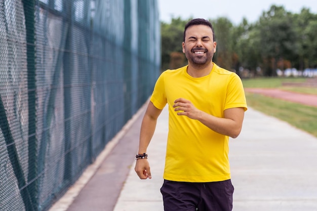 노란색 티셔츠를 입은 활기찬 남자가  ⁇ 은 여름날 훈련을 하는 도시 공원 경기장에서 조 ⁇ 을 합니다.