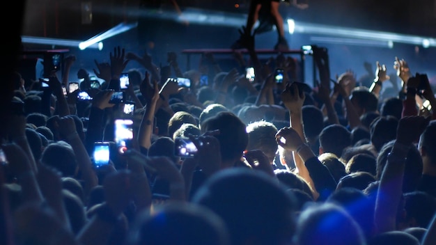 Energetic people dancing with their hands up at the punk concert blue lighting