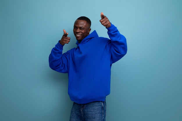 Energetic positive young african guy in a stylish hoodie is having fun with music on a studio