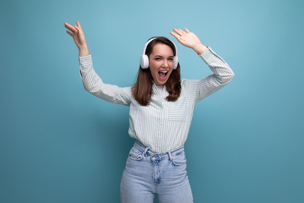 energetic pretty cute brunette young woman in shirt listening to music on studio background with copy pace