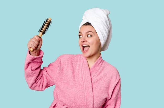 Energetic woman in a pink bathrobe ready to start the day with a towel on her head and a brush