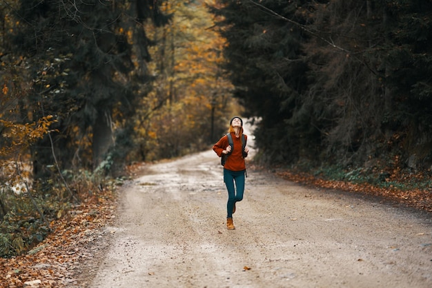 秋の森でバックパックを背負って道路に沿って走っているエネルギッシュな女性 高品質の写真