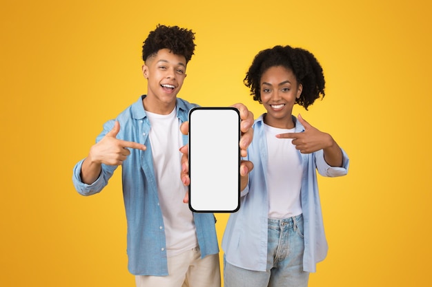 Energetic young african american couple holding and pointing at a smartphone with a blank screen