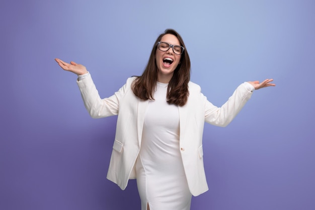 Energetic young lady in a white dress and glasses demonstrates with her hands to the sides