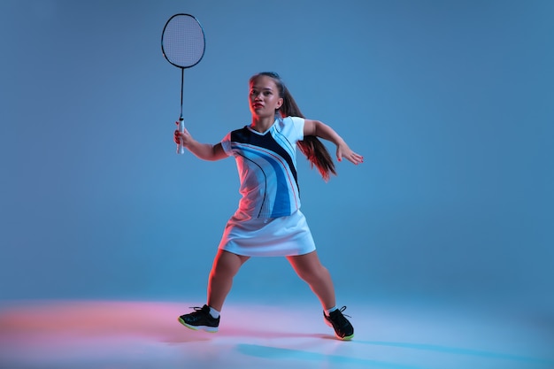 Energie. Mooie dwerg vrouw beoefenen in badminton geïsoleerd op blauwe achtergrond in neonlicht. Lifestyle van inclusieve mensen, diversiteit en gelijkheid. Sport, activiteit en beweging. Kopieerruimte.