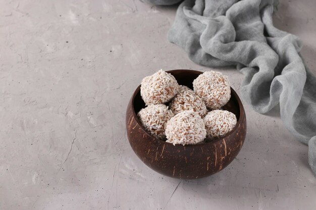 Energieballen van noten en havermout met kokosvlokken in kokosnootkom op grijze achtergrond, horizontaal formaat, exemplaarruimte