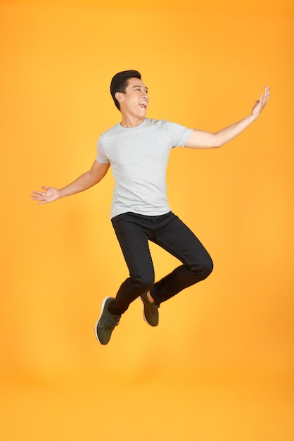 Energieke gelukkige jonge Aziatische man in casual kleding springen studio-opname geïsoleerd in oranje achtergrond