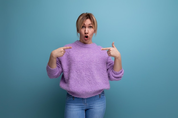 Energieke verontwaardigde blonde jonge vrouw in paarse hoodie schreeuwend van verbazing op een blauwe achtergrond