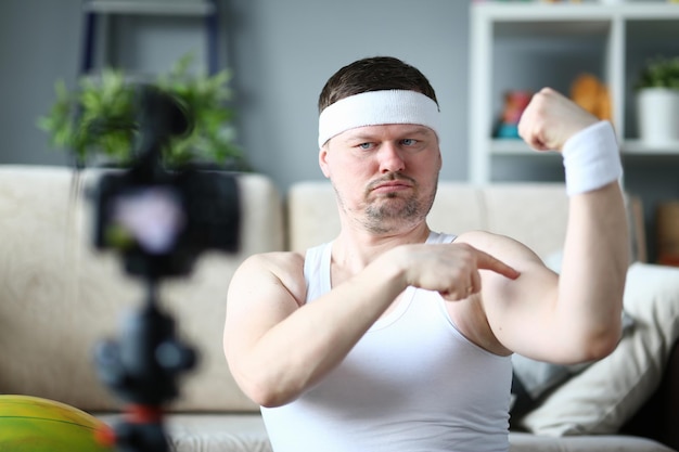 Energieke vrolijke mannelijke blogger die de grootte van de biceps meet terwijl hij glimlacht en blog bijwerkt