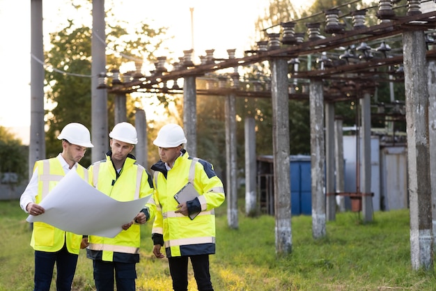 Energiespecialisten plannen een nieuw project buiten drie ingenieurs lopen in de buurt van hoogspanningslijnen