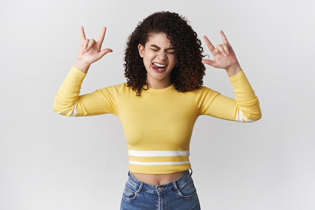 Energized extremelly happy joyful party girl having fun wearing stylish outfit show rocknroll heavy metal signs close eyes enjoy awesome music stick tongue carefree dancing white background